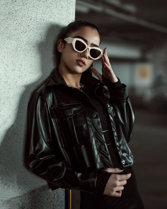 Home Fashionable woman in black leather leaning on a wall, exuding confidence.